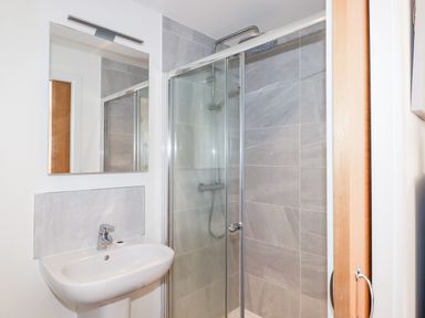 A bathroom with a sink basin under a mirror and a glass-enclosed shower with tiled walls at Pebble Ridge View in Westward Ho
