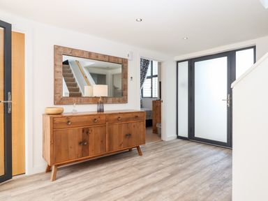 An entrance hall with a wooden sideboard a large mirror stairs and a door to a bedroom at Pebble Ridge View in Westward Ho