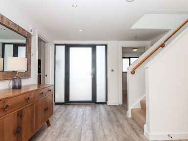 An entrance hallway with a wooden sideboard and lamp a large mirror frosted glass front door and stairs with a wooden handrail at Pebble Ridge View in Westward Ho