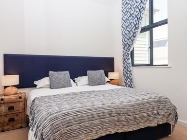 A bedroom with a bed a striped blanket two pillows two bedside tables with lamps and a window with patterned curtains at Pebble Ridge View in Westward Ho