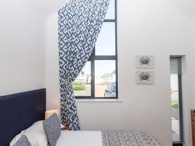 A bedroom with a bed near a tall window with blue and white curtains and two crab paintings on the wall at Pebble Ridge View in Westward Ho