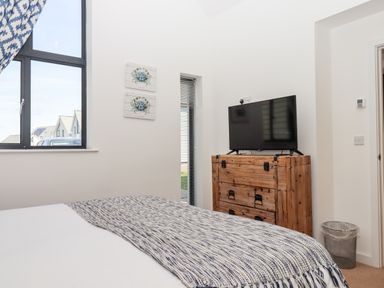 A bedroom with a bed, wooden dresser with a TV on top, two wall paintings, and a window at Pebble Ridge View in Westward Ho