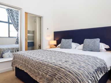 A bedroom with a bed blue headboard two pillows striped blanket bedside lamp mirror and open door to bathroom at Pebble Ridge View in Westward Ho