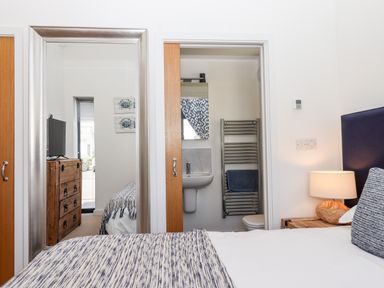 A bedroom with a bed lamp and bedside table a mirror reflecting a dresser and television and a bathroom visible through an open door at Pebble Ridge View in Westward Ho