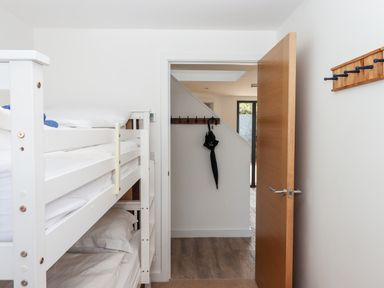 A bedroom with white bunk beds and an open wooden door showing a hallway with hooks and a black umbrella at Pebble Ridge View in Westward Ho
