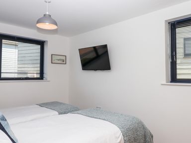 A bedroom with two single beds a wall mounted TV and two windows at Pebble Ridge View in Westward Ho