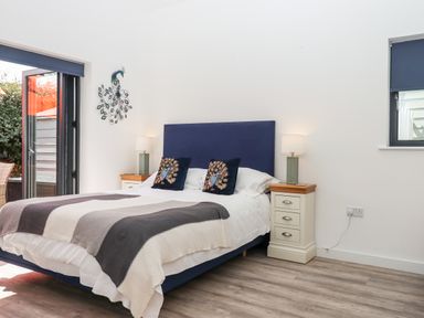 A bedroom with a bed with blue headboard and peacock cushions with bedside tables and lamps at Pebble Ridge View in Westward Ho