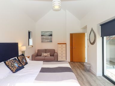 A bedroom with a bed a sofa a chest of drawers a mirror and a window with a blind at Pebble Ridge View in Westward Ho