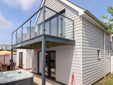 Exterior of a two-story house with a glass balcony seating area a hot tub on the patio and outdoor dining table at Pebble Ridge View in Westward Ho