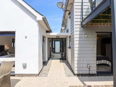 An outdoor walkway between two buildings with patio doors leading to rooms and a balcony above at Pebble Ridge View in Westward Ho