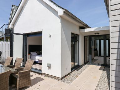 An outdoor patio with wicker chairs and a glass table outside a modern white building with open glass doors at Pebble Ridge View in Westward Ho