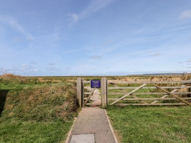 A wooden gate with a path leading through grassland under a blue sky at Pebble Ridge View in Westward Ho
