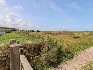 A grassy field with wildflowers a wooden fence and a gravel path under a blue sky at Pebble Ridge View in Westward Ho