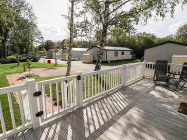 A view from a wooden deck with white railing overlooking parked caravans and trees at 18 Woodlands Retreat in Tattershall