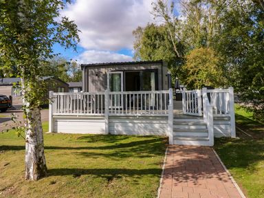 A small house with a white wooden deck and railing surrounded by grass and trees at 18 Woodlands Retreat in Tattershall