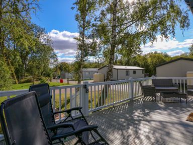 An outdoor deck with chairs and a table overlooking a residential area with trees at 18 Woodlands Retreat in Tattershall