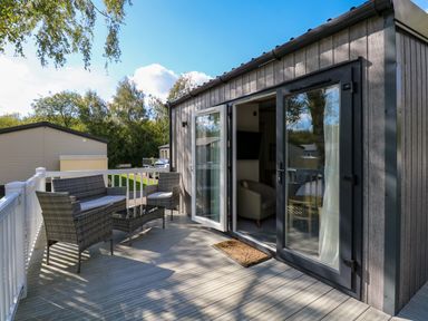 An outdoor deck with wicker furniture including a sofa and chairs beside a building with open glass doors at 18 Woodlands Retreat in Tattershall
