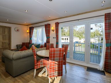 A living room with a round dining table and plaid chairs near large glass doors at 18 Woodlands Retreat in Tattershall