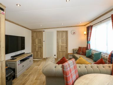 A living room with a large sectional sofa with cushions a wall mounted television wooden doors and a table at 18 Woodlands Retreat in Tattershall