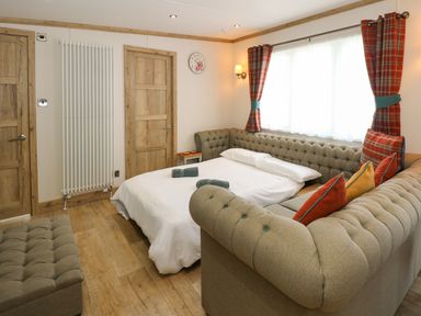 A bedroom with a pull-out bed sofa with pillows wooden floor two wooden doors and a window with red plaid curtains at 18 Woodlands Retreat in Tattershall