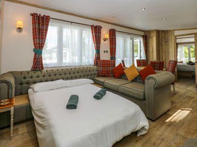 A living room with a fold-out bed sofa chairs and plaid curtains at 18 Woodlands Retreat in Tattershall