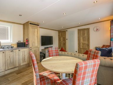 A kitchen and dining area with wooden cabinets a round wooden table and four plaid chairs at 18 Woodlands Retreat in Tattershall