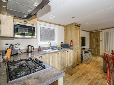 A kitchen and living area with wooden cabinets a gas stove and a television at 18 Woodlands Retreat in Tattershall