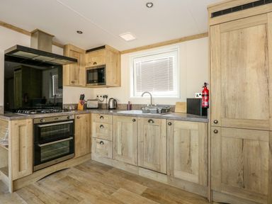 A kitchen with wooden cabinets a double oven a gas stove a microwave toaster kettle and a sink at 18 Woodlands Retreat in Tattershall
