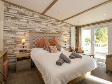A bedroom with a bed with pillows and rolled towels two nightstands wall lamps a radiator two armchairs a small table and sliding glass doors at 18 Woodlands Retreat in Tattershall