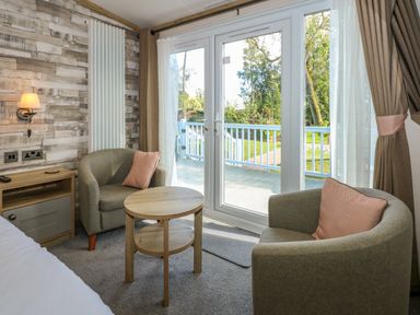 A seating area with two chairs a round wooden table and a side table next to glass doors at 18 Woodlands Retreat in Tattershall