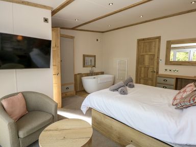 A bedroom with a bed pillows towels armchair table bathtub television and wooden furniture at 18 Woodlands Retreat in Tattershall