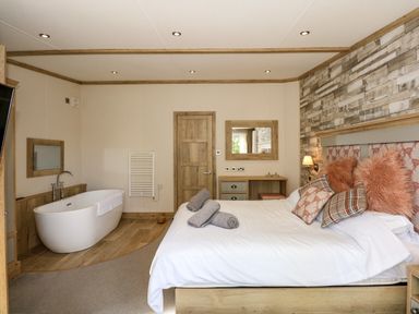 A bedroom with a bed, cushions, towels, a bathtub, a desk, a mirror, and a wooden door at 18 Woodlands Retreat in Tattershall