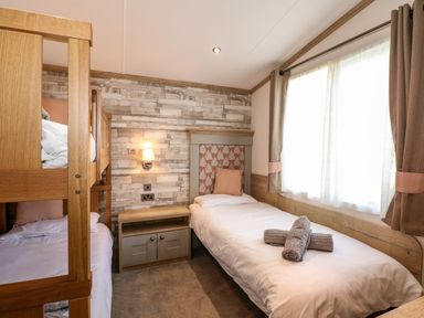 A bedroom with bunk beds a single bed a nightstand and a window at 18 Woodlands Retreat in Tattershall