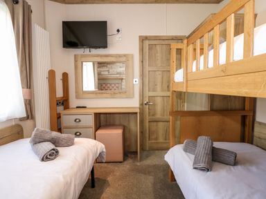 A bedroom with a bunk bed and a single bed with rolled towels a desk and a wall mounted TV at 18 Woodlands Retreat in Tattershall