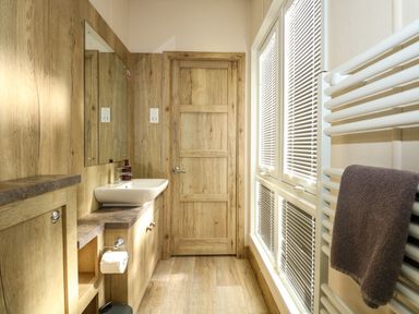 A bathroom with a wooden door a wall-mounted sink a mirror blinds on windows and a towel on a white radiator at 18 Woodlands Retreat in Tattershall