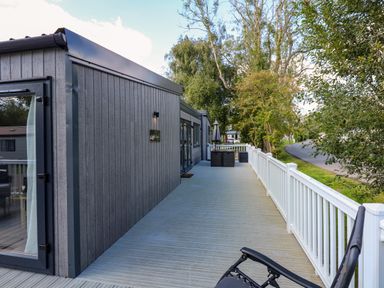 An outdoor deck with railing attached to a modern gray building with trees and road in the background at 18 Woodlands Retreat in Tattershall