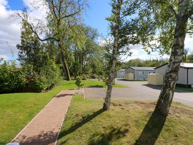 A paved path through a grassy area with trees and several small buildings at 18 Woodlands Retreat in Tattershall