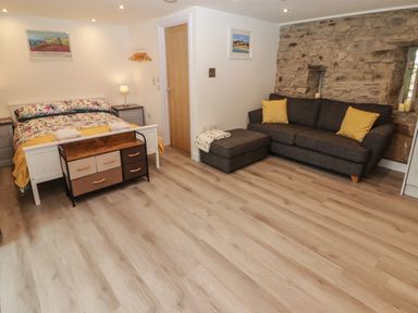 A bedroom with a bed a sofa ottoman and a stone wall at The Nest in Amroth
