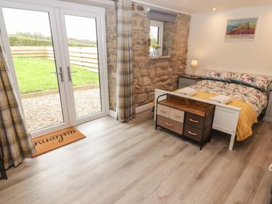 A bedroom with a double bed side tables a storage bench and French doors leading outside at The Nest in Amroth
