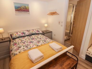 A bedroom with a double bed with floral bedding and folded towels on a yellow blanket at The Nest in Amroth