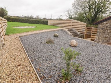 A fenced garden area with gravel and stones next to a stone building at The Nest in Amroth