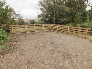 An empty gravel area with a wooden fence and trees in the background at The Nest in Amroth