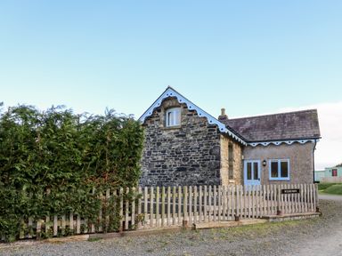 A stone and plaster house with blue trim and a wooden fence with bushes behind at Railway Station Cottage in New Radnor near Kington