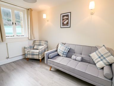 A small sitting room with a grey sofa and plaid armchair near a window at Railway Station Cottage in New Radnor near Kington