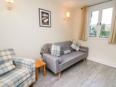 A sitting area with a gray sofa, a plaid armchair, a small wooden table with two glasses, and a window at Railway Station Cottage in New Radnor near Kington