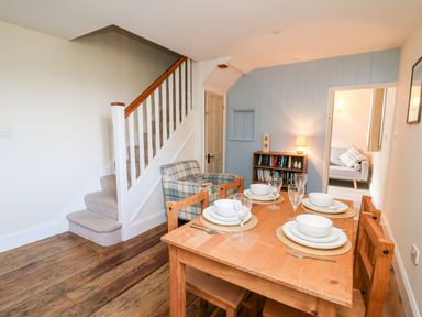 A dining area with a wooden table set for four near a staircase and a small sitting area at Railway Station Cottage in New Radnor near Kington