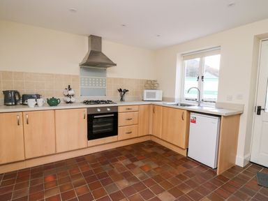 A kitchen with wooden cabinets a gas stove oven microwave and small fridge under the counter at Railway Station Cottage in New Radnor near Kington