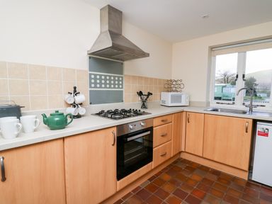 A kitchen with wooden cabinets a gas stove microwave kettle and coffee mugs at Railway Station Cottage in New Radnor near Kington