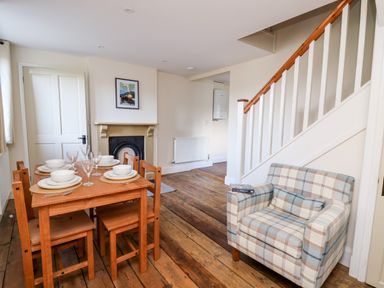 A dining area with a wooden table set for four next to a plaid armchair near stairs at Railway Station Cottage in New Radnor near Kington