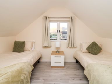 A bedroom with two single beds separated by a nightstand with a lamp under a window with curtains at Railway Station Cottage in New Radnor near Kington
